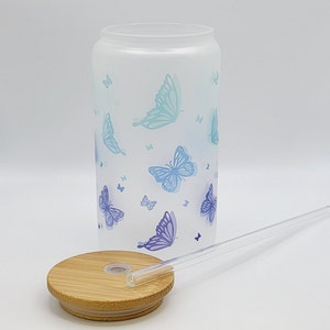 Glas mit blauen Schmetterlingen von vorne, daneben der Bambusdeckel und darauf liegt ein Glasstrohhalm.