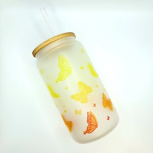 Milchglas mit Bambusdeckel und Glasstrohalm mit Schmetterlingen von Gelb zu Orange verlaufend.