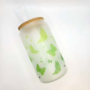 Milchglas mit Bambusdeckel und Glasstrohalm mit Schmetterlingen von Hellgrün zu Grün verlaufend.