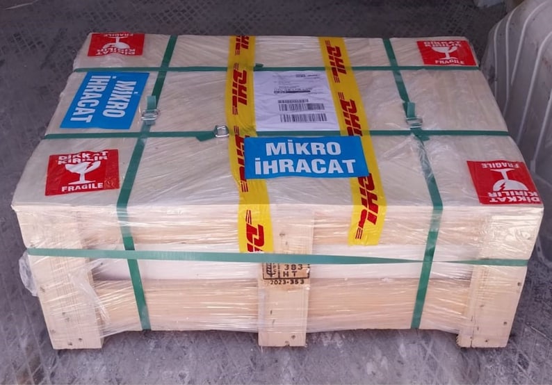 K&ouml;nnte beinhalten: Ein Holzkasten mit gelbem und schwarzem DHL-Klebeband, einem blauen Etikett mit der Aufschrift "Mikro Ihracat" und einem roten Etikett mit der Aufschrift "Dikkat Kırılabilir Fragile".