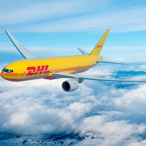 May include: A yellow DHL cargo airplane flies through a cloudy sky. The plane has the DHL logo in red and yellow on its side. The wings are extended, and the plane is in mid-flight.
