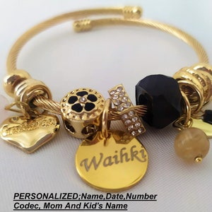 May include: Gold charm bracelet with a variety of charms, including a heart, a flower, a star, and a bead. The bracelet also has a personalized tag with the name "Waihki".