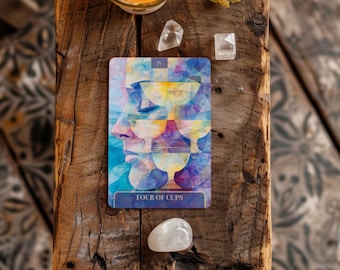May include: A tarot card with a blue, yellow, and purple design featuring a profile and four cups. The card is labeled "FOUR OF CUPS" and is on a rustic wooden surface. Crystals and a lit candle are also present.