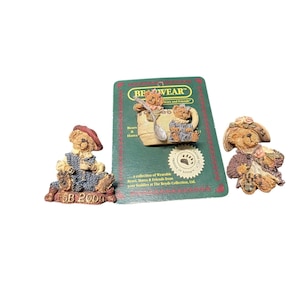 Puede incluir: Tres figuras de osos coleccionables. Un oso está sentado, con un atuendo azul y una boina roja. Otro oso está en una taza de té con una cuchara. El tercer oso lleva un sombrero y un chal floral. La tarjeta verde dice "BEWEAR Bears and Hares".