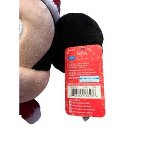 Op de afbeelding: Een Mickey Mouse pluche speelgoed met een kerstmuts en rood-witte afwerking. Het speelgoed heeft een zwart oor en een rood label met het woord "Mickey" en het telefoonnummer 1-800-317-3245.