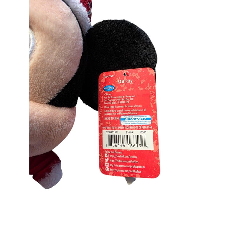 Op de afbeelding: Een Mickey Mouse pluche speelgoed met een kerstmuts en rood-witte afwerking. Het speelgoed heeft een zwart oor en een rood label met het woord "Mickey" en het telefoonnummer 1-800-317-3245.