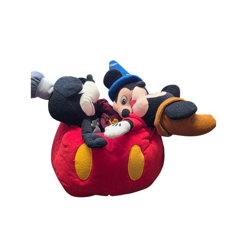 May include: A plush toy featuring Mickey Mouse, Donald Duck, and Pluto. Mickey is wearing a blue sorcerer's hat and red robe. The plush toys are inside a large red Mickey Mouse-shaped plush with yellow accents. The toys are on a white background.