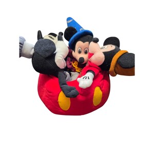 May include: A red plush Mickey Mouse-themed toy with yellow accents, holding three Mickey Mouse plush figures. One Mickey Mouse is wearing a blue wizard hat. The other two Mickey Mouse figures are black, white, and red.