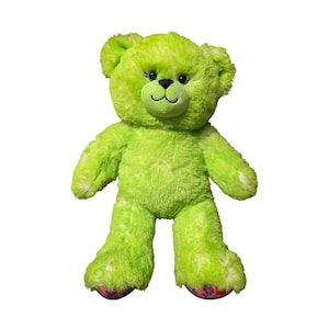 May include: A bright lime green plush teddy bear with soft, textured fur. The bear features dark blue embroidered eyes with long eyelashes, a black stitched nose and mouth, and colorful patterned fabric on the bottom of its two feet.