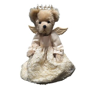 May include: A plush teddy bear dressed as an angel, featuring a cream-colored lace dress, small wings, and a gold halo. The bear has a light brown fur and a sweet expression, perfect for a nursery or as a collectible item.