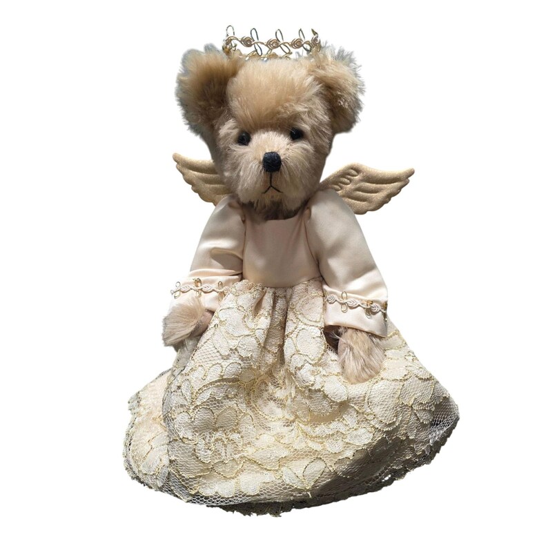 May include: A plush teddy bear dressed as an angel, featuring a cream-colored lace dress, small wings, and a gold halo. The bear has a light brown fur and a sweet expression, perfect for a nursery or as a collectible item.