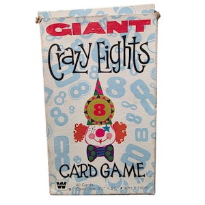May include: Vintage "Giant Crazy Eights Card Game" box. The box features a clown illustration with a red number 8 on its chest. The box is white with blue number 8s scattered across the surface. The text "Crazy Eights" is in a whimsical font.