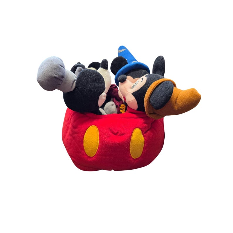 May include: A plush Mickey Mouse toy in a red, round container with yellow oval accents. Mickey Mouse is wearing a blue wizard hat and a brown and black hat. The toy is black, white, and red.