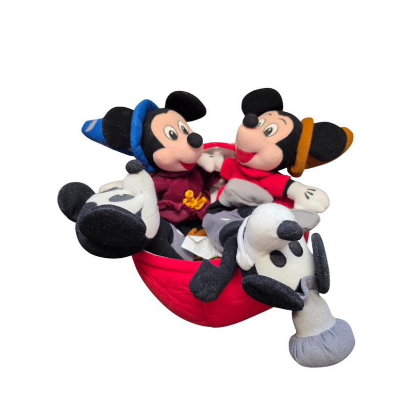 May include: A red, plush, boat-shaped container holds three stuffed toys: two Mickey Mouse figures and a Pluto figure. The Mickey Mouse figures wear red and maroon outfits with hats. The Pluto figure is black, white, and gray.