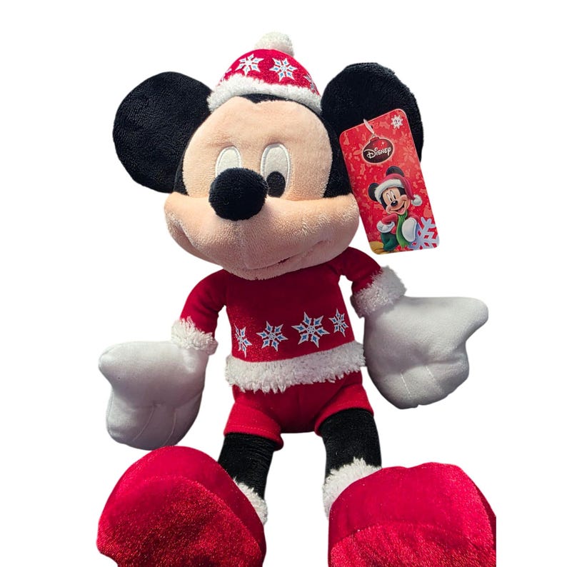 Op de afbeelding: Een pluche Mickey Mouse-speelgoed in een rood kerstoutfit met witte randen en sneeuwvlokken. Het speelgoed heeft een bijpassende hoed en grote rode voeten. Een Disney-label is bevestigd.