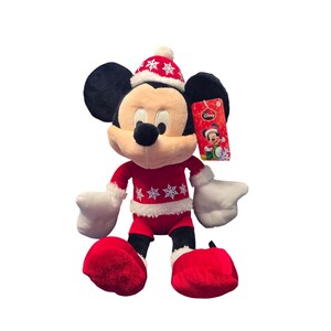 Op de afbeelding: Een pluche Mickey Mouse-speelgoed gekleed in een rood kerstoutfit met witte randen en sneeuwvlokaccenten. Het speelgoed heeft zwarte oren, een rode hoed en een label met een Disney-logo. Het speelgoed is ongeveer 30 cm hoog.