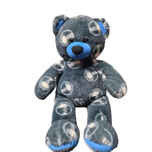 May include: A plush teddy bear featuring dark grey fur with a repeating pattern of white circular motifs. The bear has a bright blue snout, inner ears, and foot pads, along with a black nose and dark, round eyes, creating a soft, textured appearance.