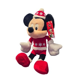 Op de afbeelding: Een pluche Mickey Mouse-speelgoed met een rood kerstoutfit met witte randen en sneeuwvlokaccenten. Het speelgoed heeft zwarte oren, een zwarte neus en witte handschoenen. Een Disney-label is bevestigd.