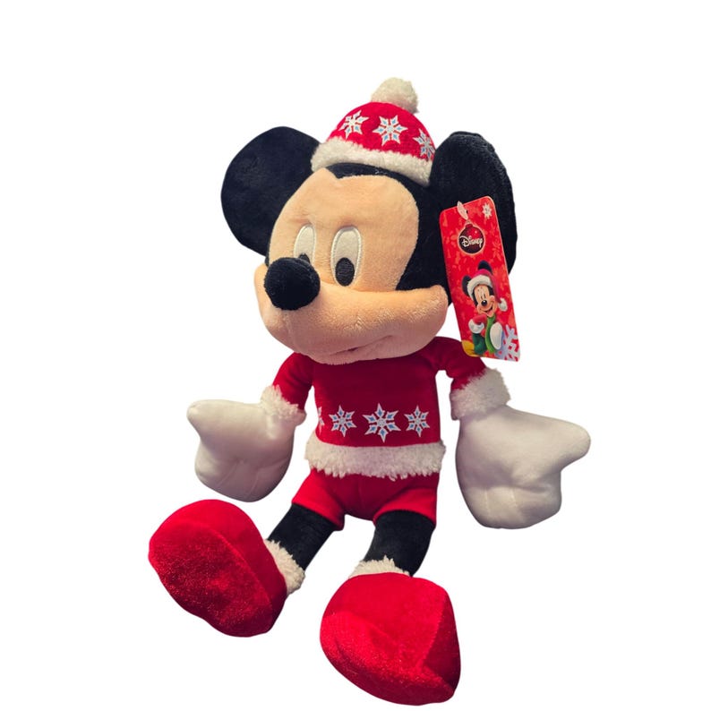 Op de afbeelding: Een pluche Mickey Mouse-speelgoed met een rood kerstoutfit met witte randen en sneeuwvlokaccenten. Het speelgoed heeft zwarte oren, een zwarte neus en witte handschoenen. Een Disney-label is bevestigd.