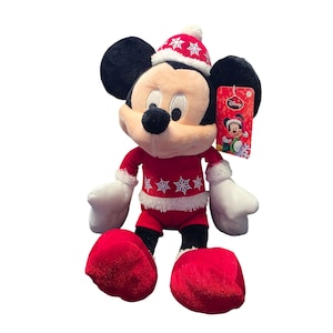 Op de afbeelding: Een pluche Mickey Mouse-speelgoed in een feestelijke kerstoutfit. De rode outfit heeft witte sneeuwvlokaccenten en -afwerking, met een bijpassende hoed. Het speelgoed heeft zwarte oren, een zwarte neus en witte handschoenen en voeten. Een Disney-label is bevestigd.