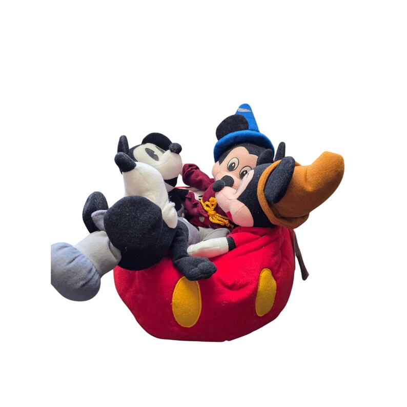 May include: A collection of Mickey Mouse plush toys, including one dressed as a sorcerer, are nestled inside a large red plush bag with yellow accents. The toys are black, white, red, and blue.
