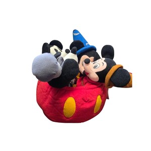 May include: A collection of Mickey Mouse plush toys, including one dressed as a sorcerer. The plush toys are in a red container with yellow circular accents. The Mickey Mouse toys have black ears, black and white faces, and black and white gloves.