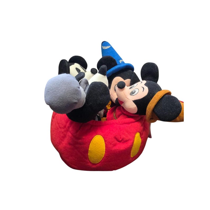 May include: A collection of Mickey Mouse plush toys, including one dressed as a sorcerer. The plush toys are in a red container with yellow circular accents. The Mickey Mouse toys have black ears, black and white faces, and black and white gloves.