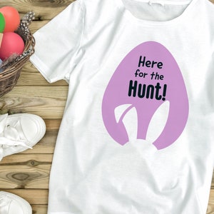 May include: White t-shirt with a purple Easter egg graphic and the text "Here for the Hunt!"