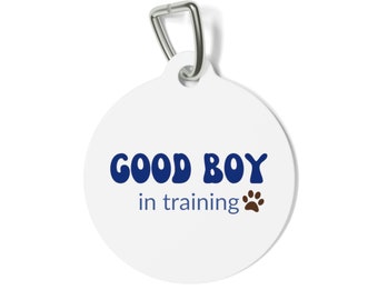 May include: White round dog tag with a blue "GOOD BOY" in a retro font and "in training" text with a brown paw print.