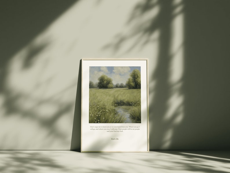 Op de afbeelding: Een ingelijste print van een schilderij dat een groene weide met een klein beekje erdoorheen afbeeldt. De lucht is blauw met witte wolken. De print bevat een citaat uit de Bijbel: "Ween niet over mij dat ik je verlaat, of keer niet van je af. Waar je heen gaat, zal ik gaan, en waar je blijft, zal ik blijven. Je volk zal mijn volk zijn en je God mijn God." - Ruth 1:16