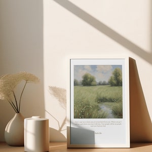 Op de afbeelding: Een ingelijste print met een schilderij van een groen veld met een beek die er doorheen loopt. De print bevat een citaat uit de Bijbel: "Dring me niet om je te verlaten of om van je terug te keren. Waar je heen gaat, ga ik heen, en waar je blijft, blijf ik. Je volk zal mijn volk zijn en je God mijn God." - Ruth 1:16.