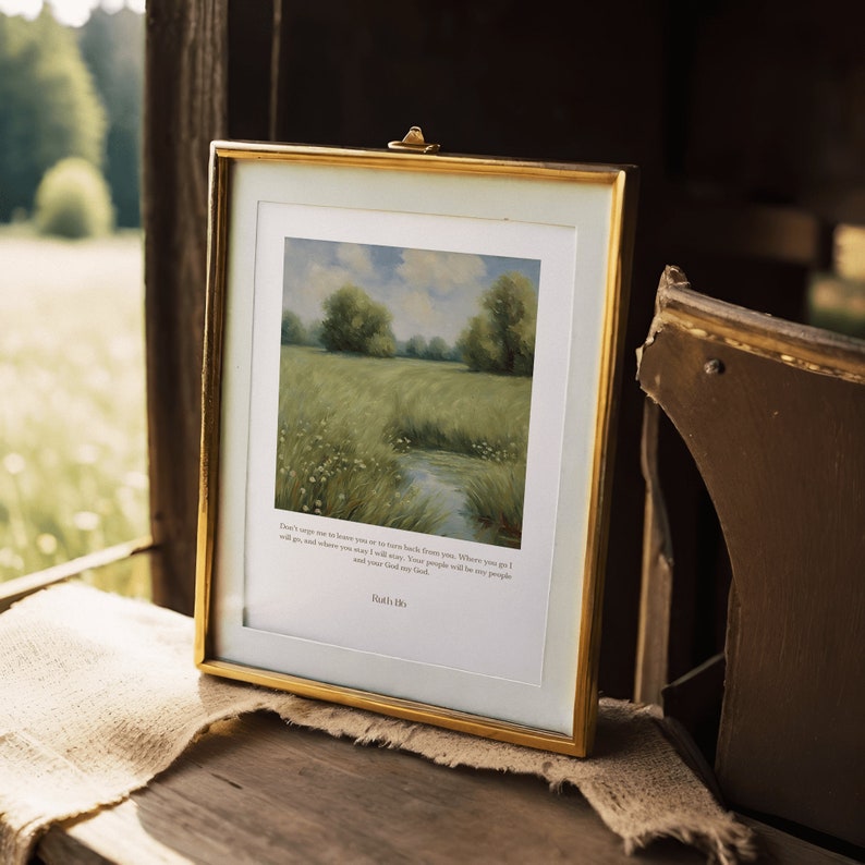 Op de afbeelding: Een gouden ingelijste print met een schilderij van een groen veld met een beek die er doorheen loopt. De print bevat een citaat uit de Bijbel: "Maak je geen zorgen, ik zal je niet alleen laten om dit te doorstaan. Ik zal bij je zijn. Waar je ook heen gaat, ik zal gaan, en waar je blijft, zal ik blijven. Je volk zal mijn volk zijn en jouw God mijn God." - Ruth 1:16