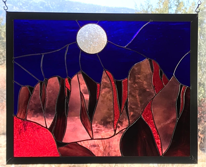 May include: A stained glass window depicting a night sky with a full moon and a mountain range in shades of red, brown, and purple.