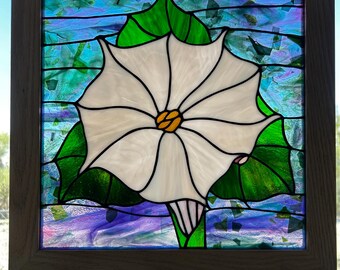May include: Stained glass panel featuring a white flower with a yellow center and black outlines, set against a backdrop of blue, green, and purple glass. The flower is framed by green leaves and encased in a wooden frame.