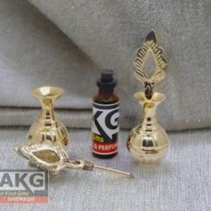 May include: Three gold-colored metal bottles with ornate tops. The bottles are small and have a round shape. One bottle has a clear glass bottle with a black cap.