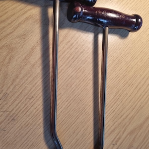 May include: Two metal boot jacks with wooden handles. The handles are dark brown and have the words "The Shoe Shop" printed on them.