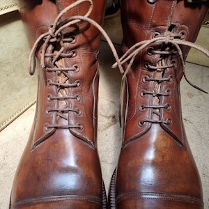 May include: A pair of brown leather boots with laces. The boots have a cap toe and are polished to a shine.