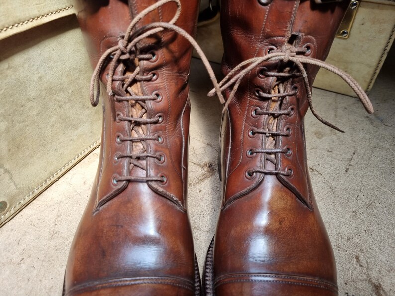 May include: A pair of brown leather boots with laces. The boots have a cap toe and are polished to a shine.