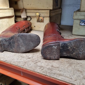 May include: A pair of brown leather riding boots with laces and buckles. The boots are worn and have scuff marks on the soles.