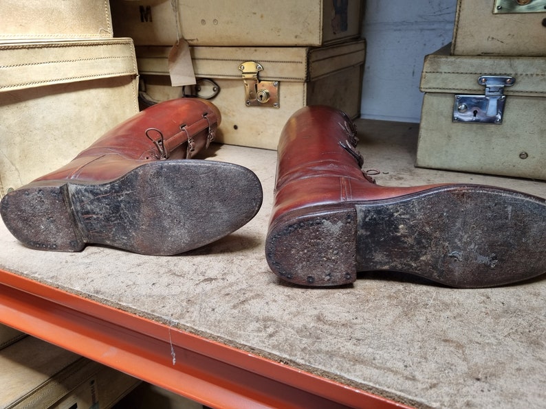 May include: A pair of brown leather riding boots with laces and buckles. The boots are worn and have scuff marks on the soles.