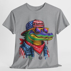 May include: Gray t-shirt featuring a cartoon alligator wearing a hat with the text "PAF0", sunglasses, a red bandana, and a denim jacket with American flag accents. The alligator has a gold chain and a pendant with the number "47".