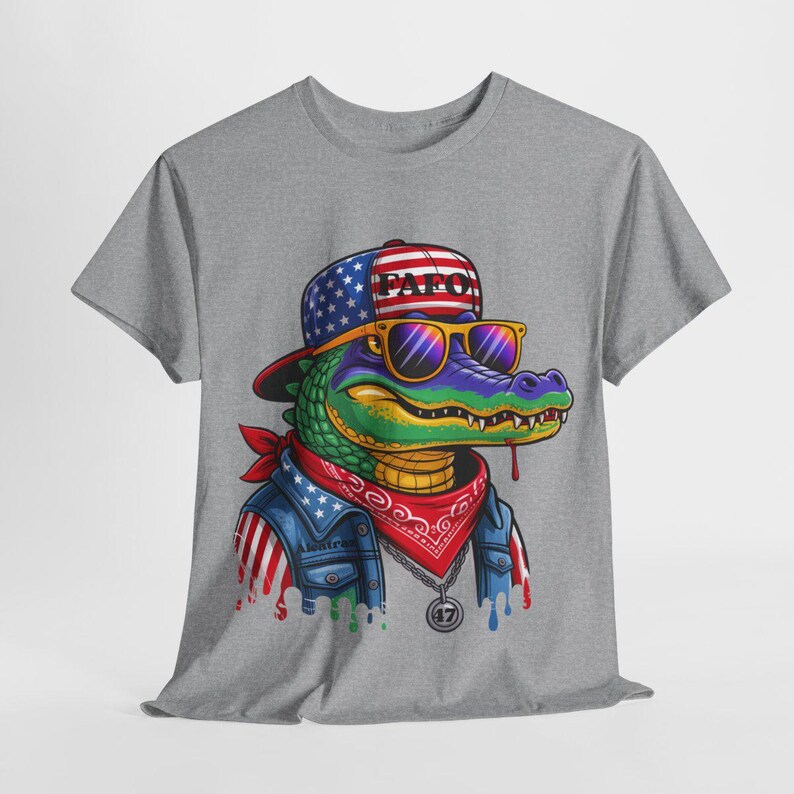 May include: Gray t-shirt featuring a cartoon alligator wearing a hat with the text "PAF0", sunglasses, a red bandana, and a denim jacket with American flag accents. The alligator has a gold chain and a pendant with the number "47".