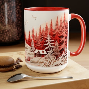 May include: White ceramic mug with a red rim and handle. The mug features a paper cut-out design of a winter scene with a red cabin in a forest of red trees.