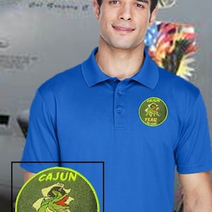 May include: A blue polo shirt with a green and yellow embroidered patch featuring a cartoon alligator with the text "CAJUN FEAR 60-0052".
