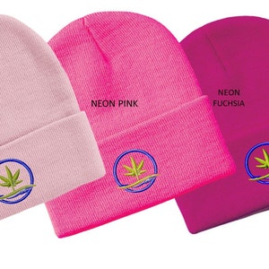 Puede incluir: Tres gorros de punto en rosa, rosa ne&oacute;n y fucsia ne&oacute;n con un logotipo de hoja de marihuana verde en un c&iacute;rculo azul. Los gorros est&aacute;n doblados.