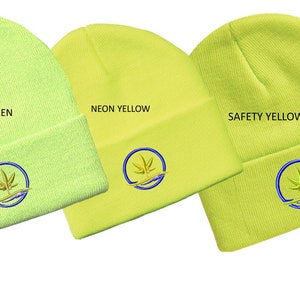 Puede incluir: Tres gorros de punto en diferentes tonos de amarillo: verde ne&oacute;n, amarillo ne&oacute;n y amarillo de seguridad. Cada gorro tiene un logotipo bordado circular con una hoja verde estilizada y una ola azul.