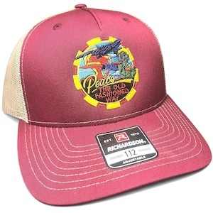 May include: Burgundy Richardson 112 trucker hat with a tan mesh back. The front features an embroidered patch with the word "Peace" and the phrase "The Old Fashioned Way". Adjustable fit.