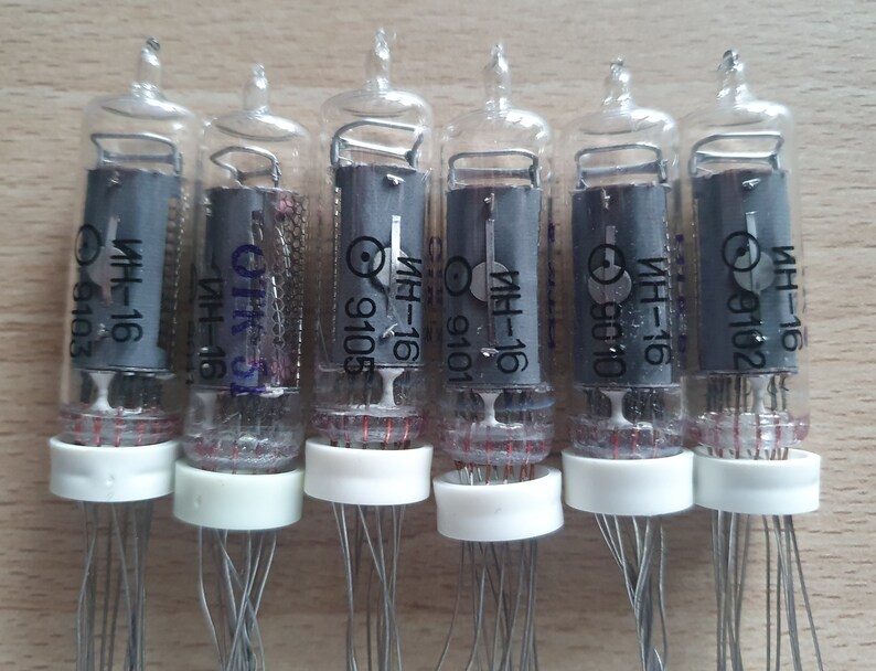 Może przedstawiać: Sześć przezroczystych szklanych lamp pr&oacute;żniowych z srebrnymi drutami i białymi czapkami. Każda lampa ma czarną etykietę z tekstem "ИН-16" i numerem, takim jak "9102" lub "9105".