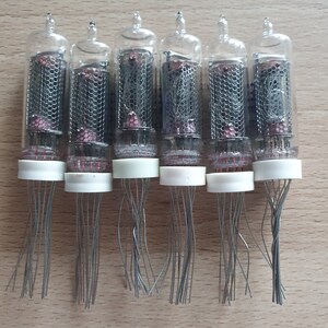 Może przedstawiać: Siedem zabytkowych szklanych lamp pr&oacute;żniowych z przezroczystym szklanym korpusem i metalową siatką wewnątrz. Lampy mają białą plastikową podstawę z wieloma cienkimi drutami wystającymi z podstawy.