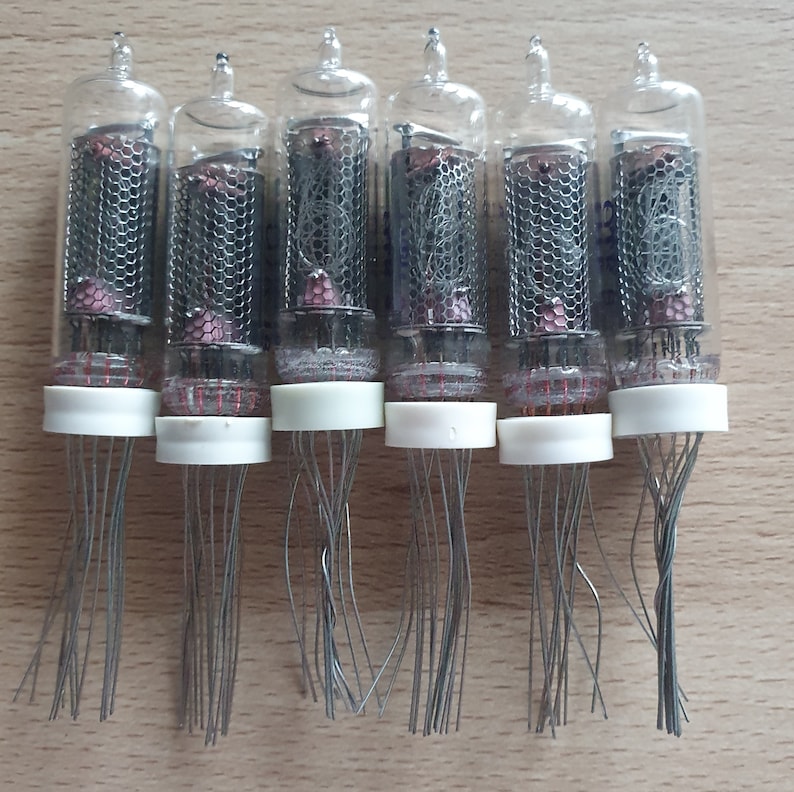 Może przedstawiać: Siedem zabytkowych szklanych lamp pr&oacute;żniowych z przezroczystym szklanym korpusem i metalową siatką wewnątrz. Lampy mają białą plastikową podstawę z wieloma cienkimi drutami wystającymi z podstawy.